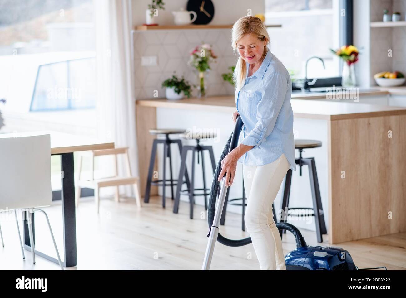Portrait of senior woman with vacuum cleaner indoors at home, hoovering. Stock Photo