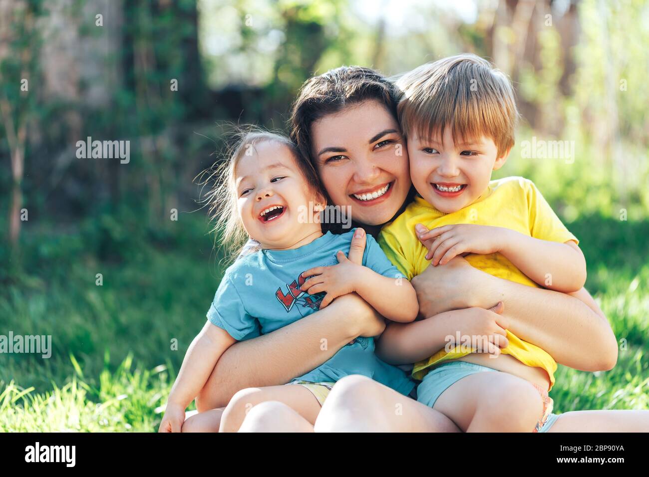 Young beautiful mother with son and daughter sit on an open-air lawn on a sunny day Stock Photo