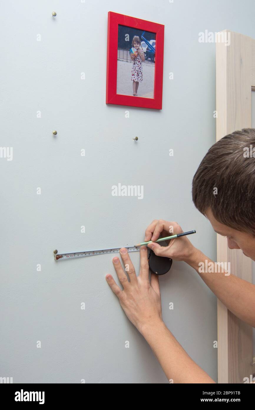 A man marks the location of the nails on the wall in order to hang