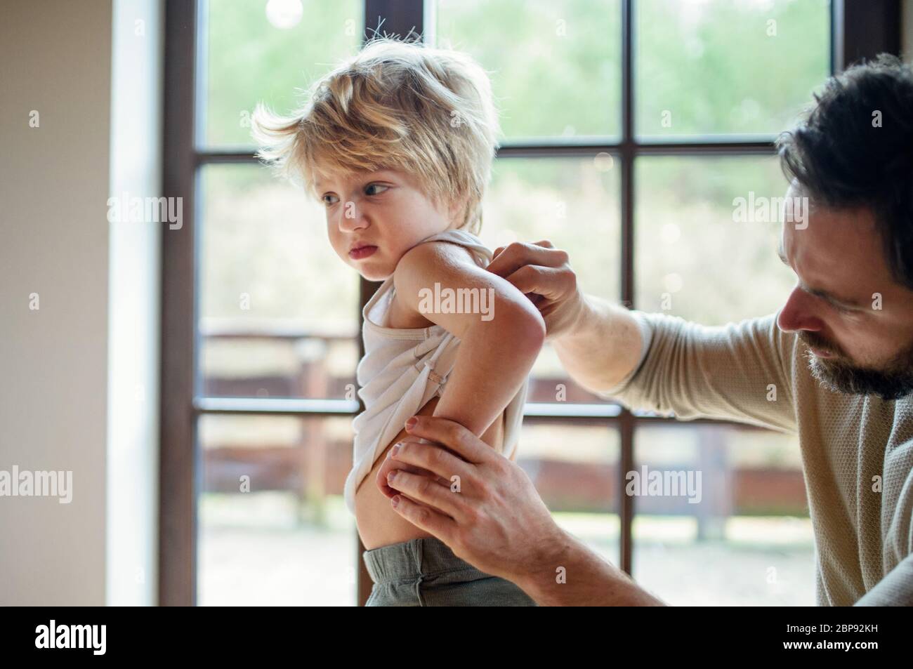 Father with small sick unhappy son indoors at home, checking his back. Stock Photo