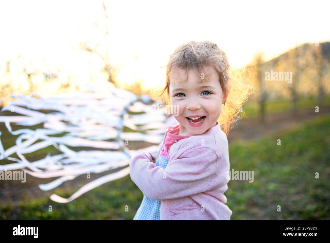 Small toddler girl standing outdoors in orchard in spring, holding hand ribbon ring. Stock Photo