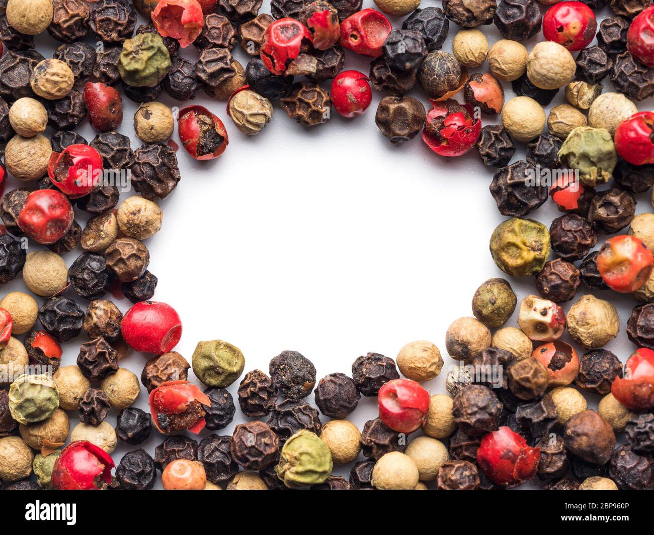 Mixed peppercorns background with white copy space in center. Food background with peppercorns. Different colored peppercorns pattern on white backgro Stock Photo