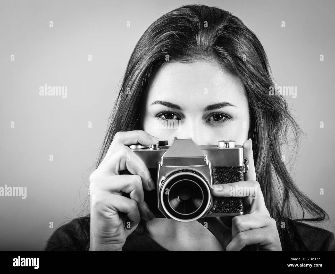 Photo of a beautiful woman pointing a vintage camera done in black and white. Stock Photo