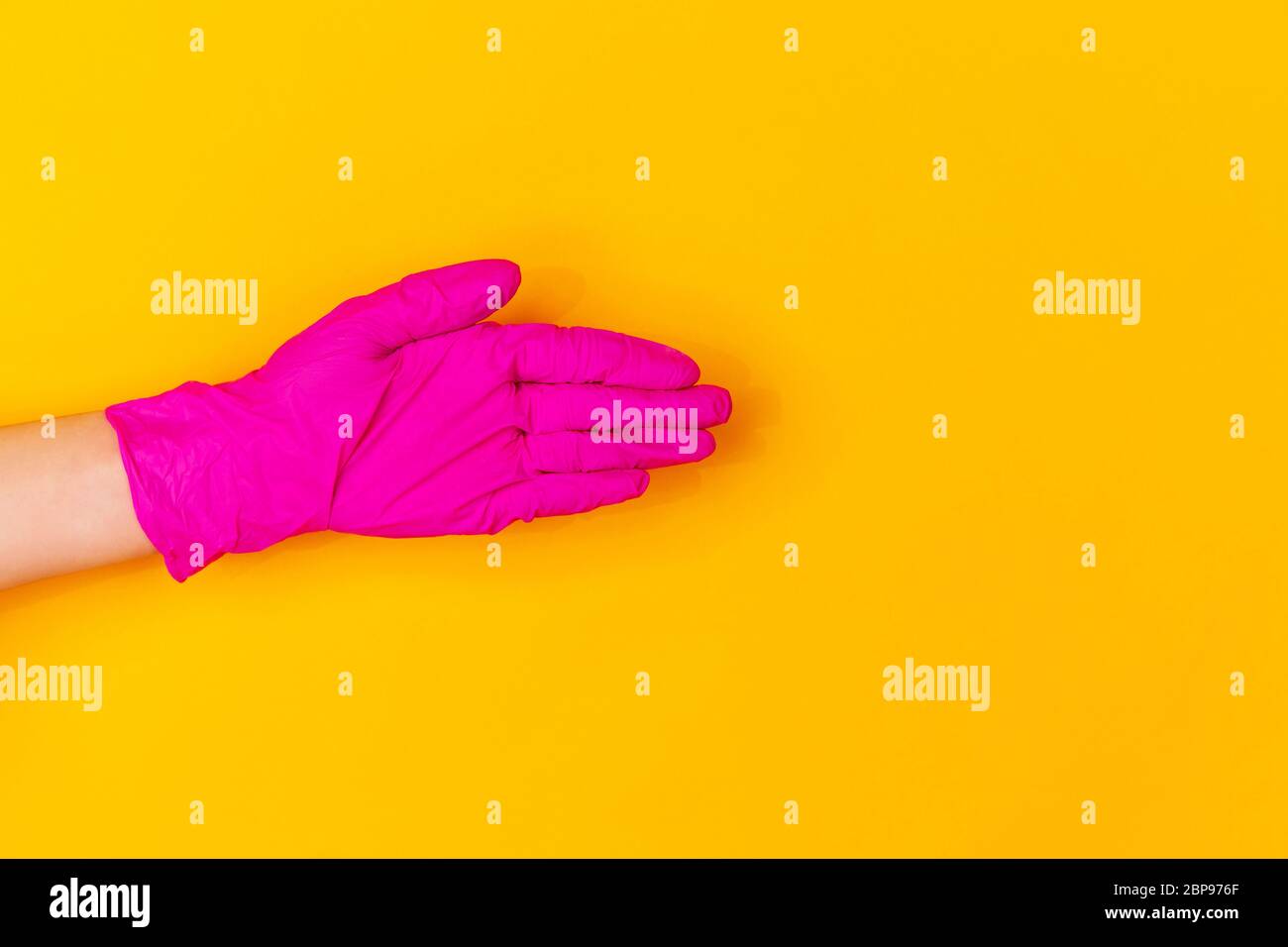 Hand in pink protective rubber glove greeting isolated on yellow studio ...