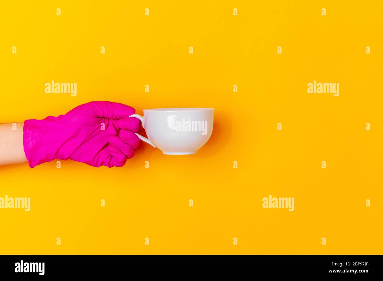 Hand in pink protective rubber glove with coffee cup isolated on yellow ...
