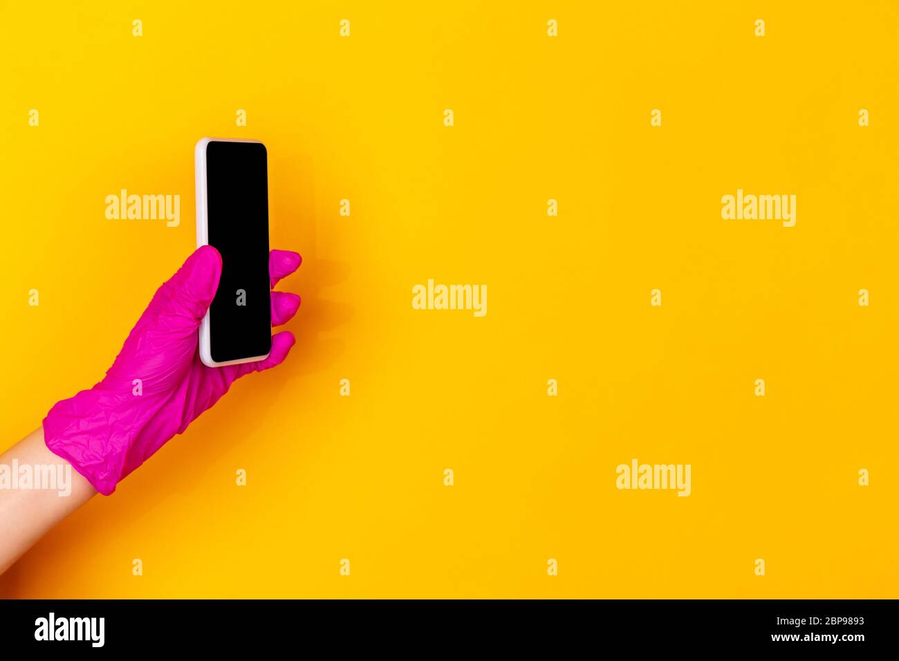 Hand in pink protective rubber glove with smartphone isolated on yellow ...