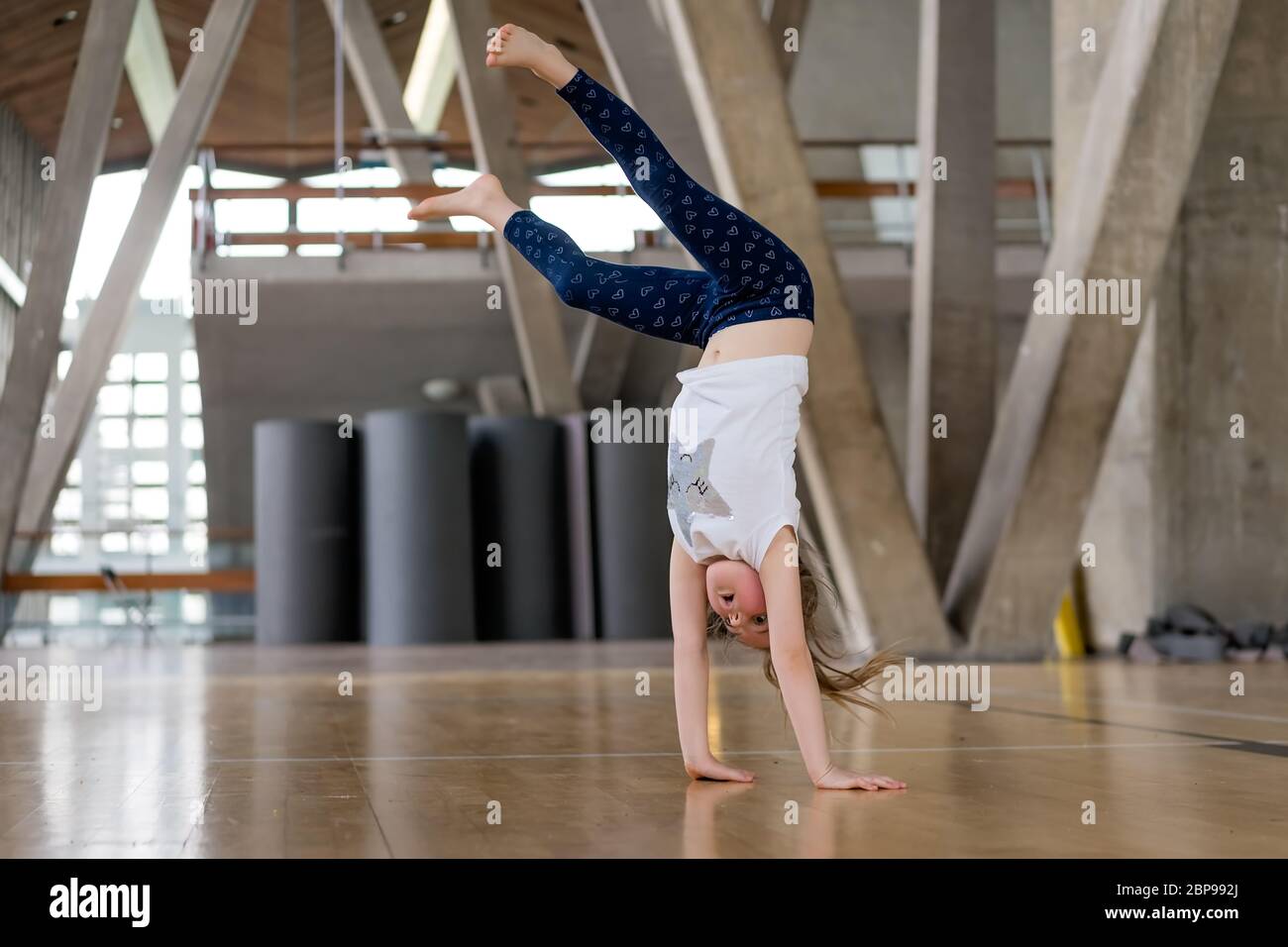 Young Caucasian girl doing cartwheel on the floor in an indoor sports centre Stock Photo