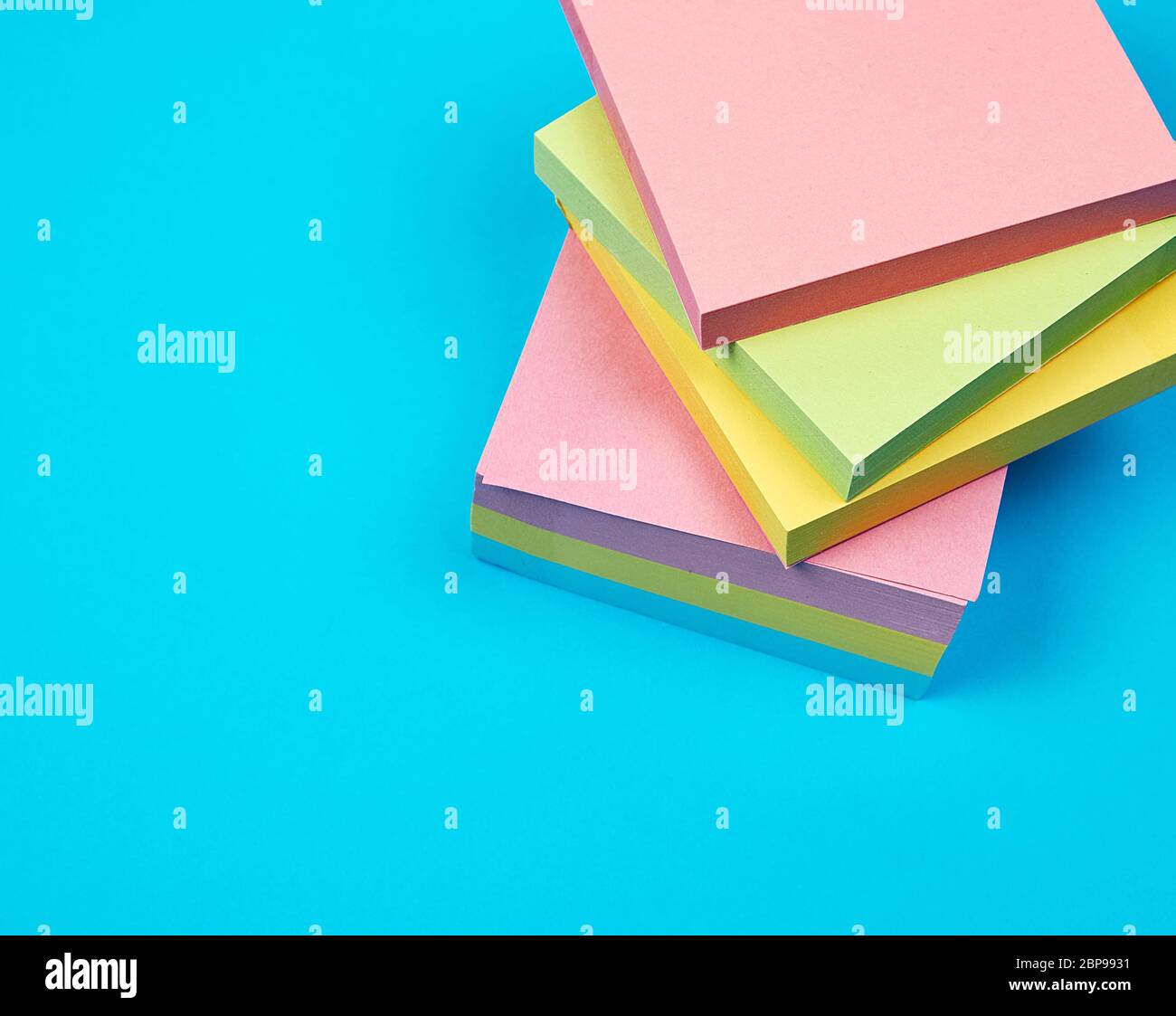 stack of multicolored empty paper square stickers on a blue background, close up Stock Photo