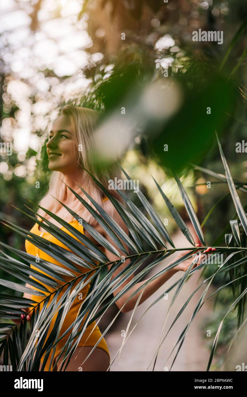 pacified sensul caucasian woman with blonde hair,slim body, closed eyes, wearing yellow swimsuit, posing on backdrop of tropical plant at sunset. Beau Stock Photo
