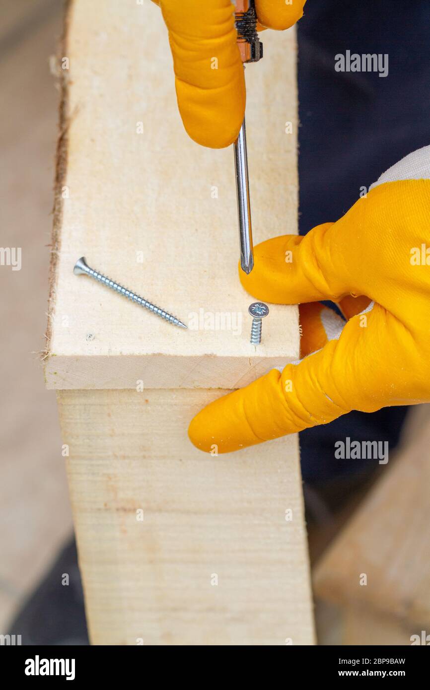 Crop view driving selftapping screw into chipboard placed on wooden