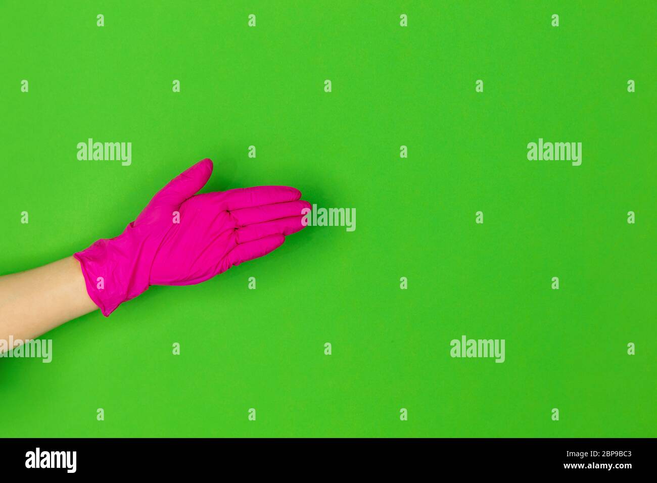 Hand in pink protective rubber glove greeting isolated on green studio ...