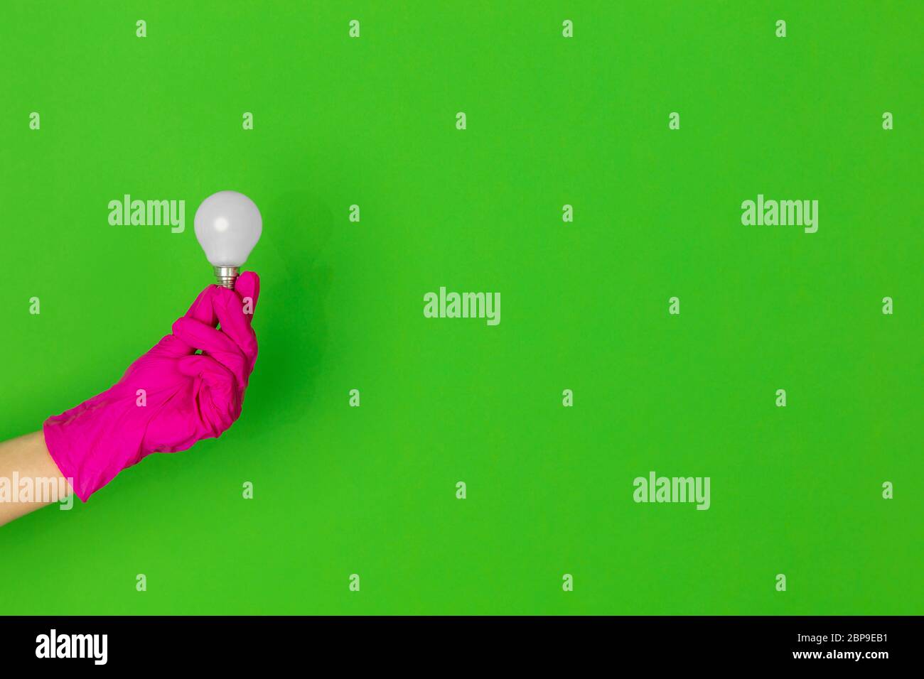 Hand in pink protective rubber glove with lightbulb isolated on green ...