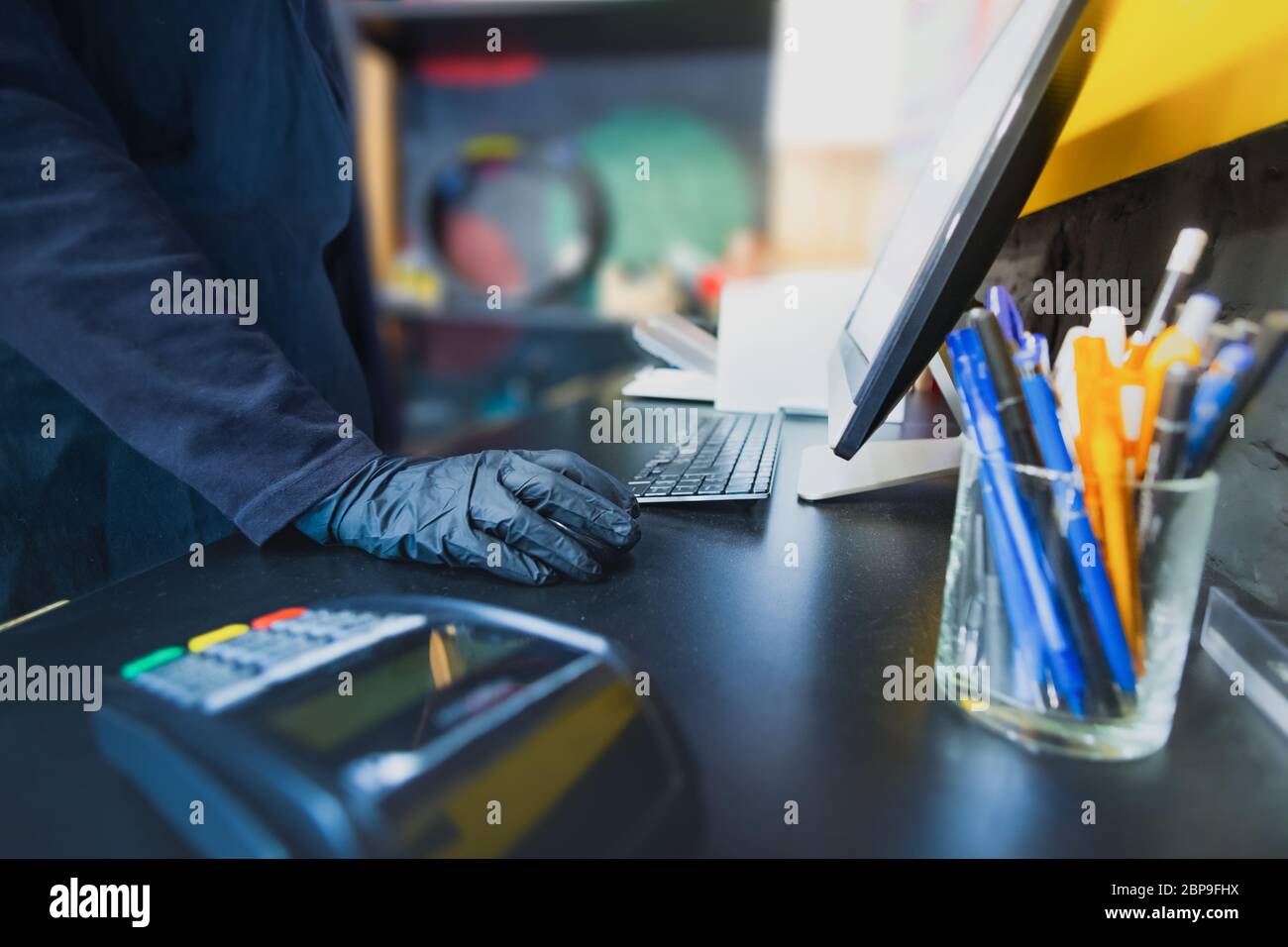Hand of a store manager at cashier desk of a generic shop. Desktop with a computer and POS terminal, small local business concept Stock Photo