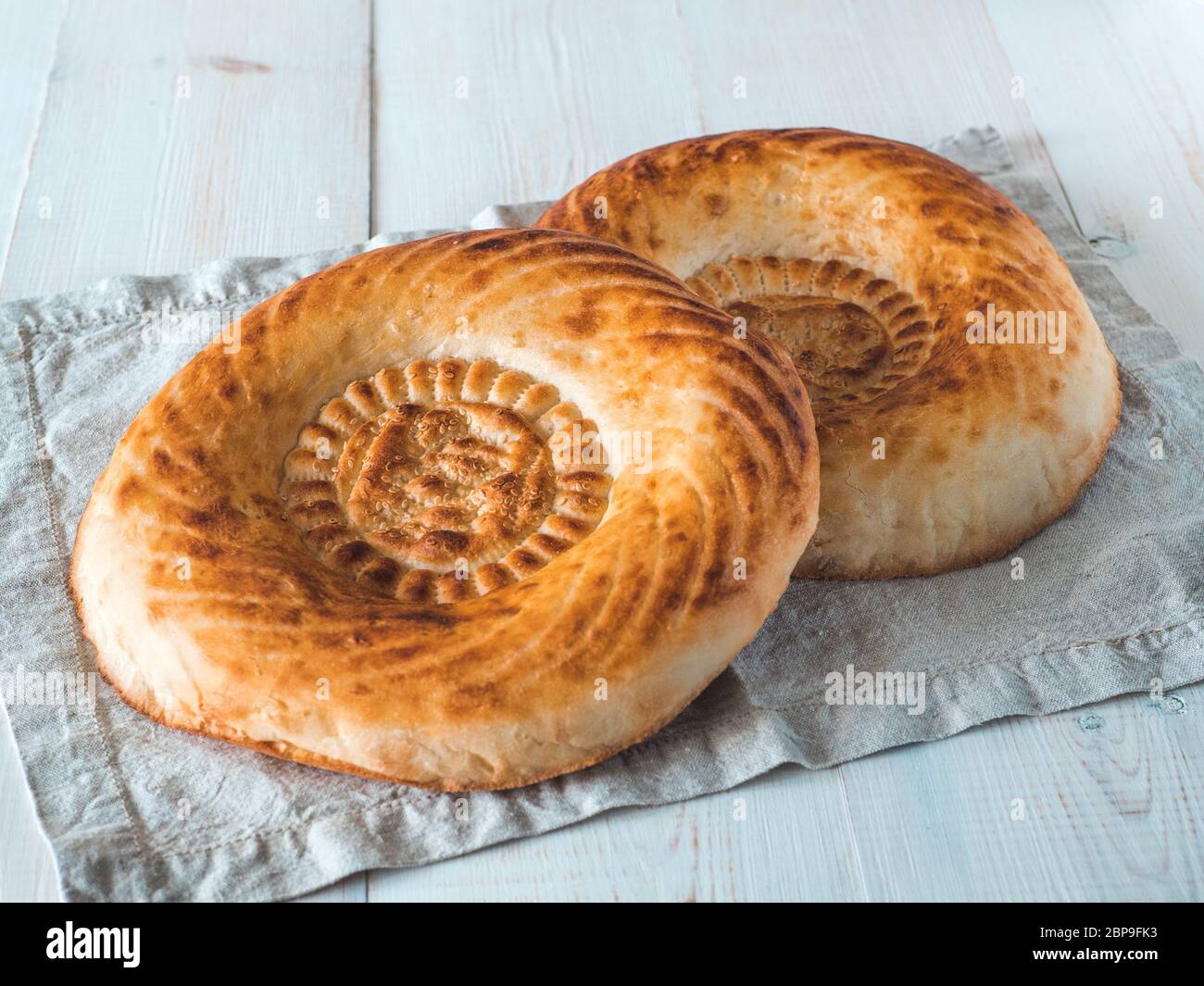 Tasty fresh tandoor bread on white wooden table. Two tandoor flat bread cake on linen kitchen towel or napkin. National asian meal, food, bread. Stock Photo