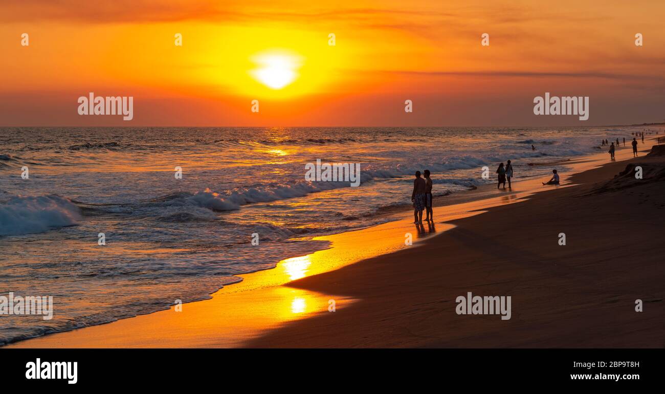 Sunset panorama along the volcanic sand beach of Monterrico with people by the Pacific Ocean, Guatemala. Stock Photo