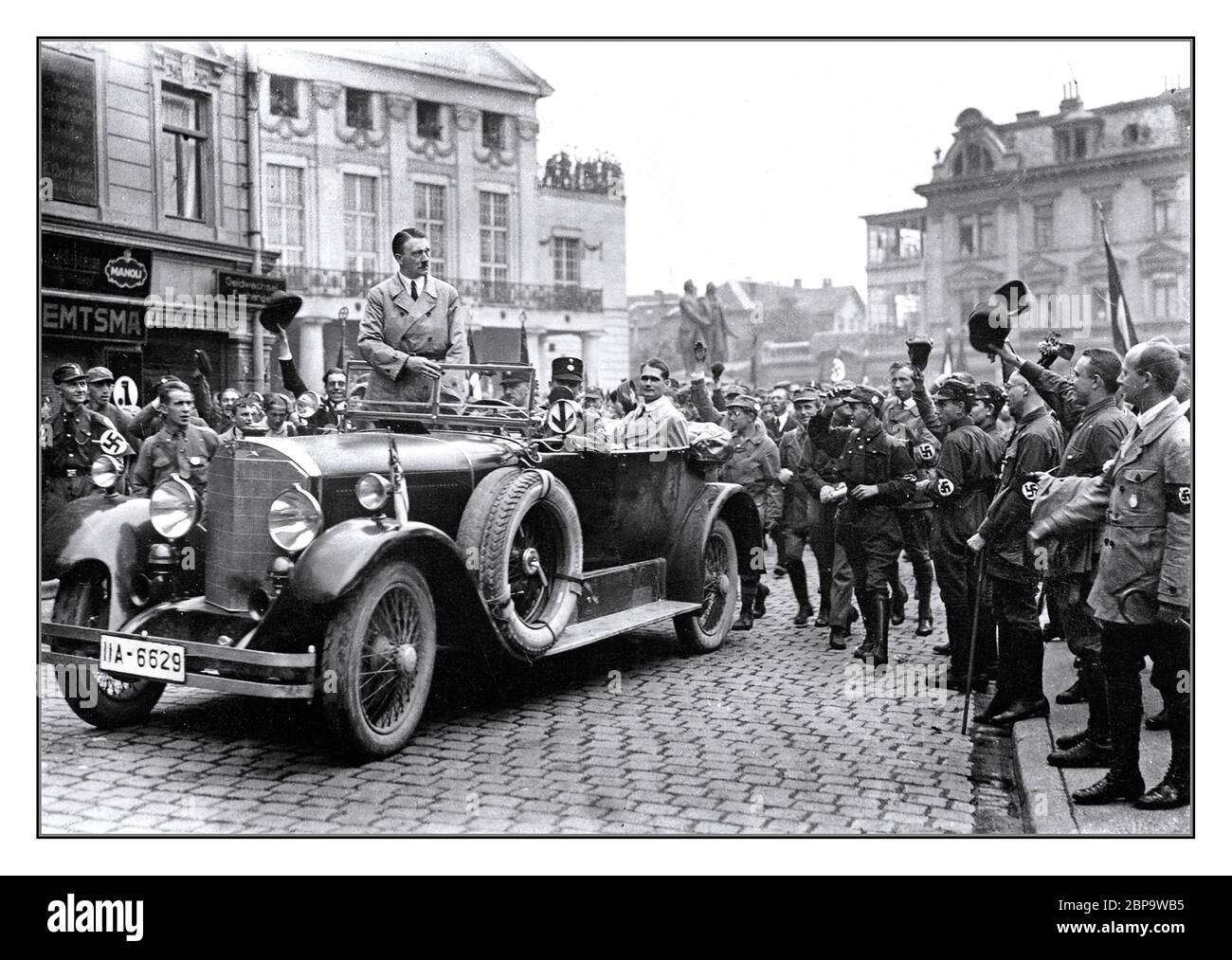 Adolf Hitler 1920’s Rally NSDAP Nazi Party pre election rally in Weimar Germany 3–4 July 1926, Hitler wearing civilian clothes standing in his open top Mercedes limousine motorcar with Rudolf Hess seated in the rear of the car. Various swastika armband wearing supporters cheering his arrival Stock Photo
