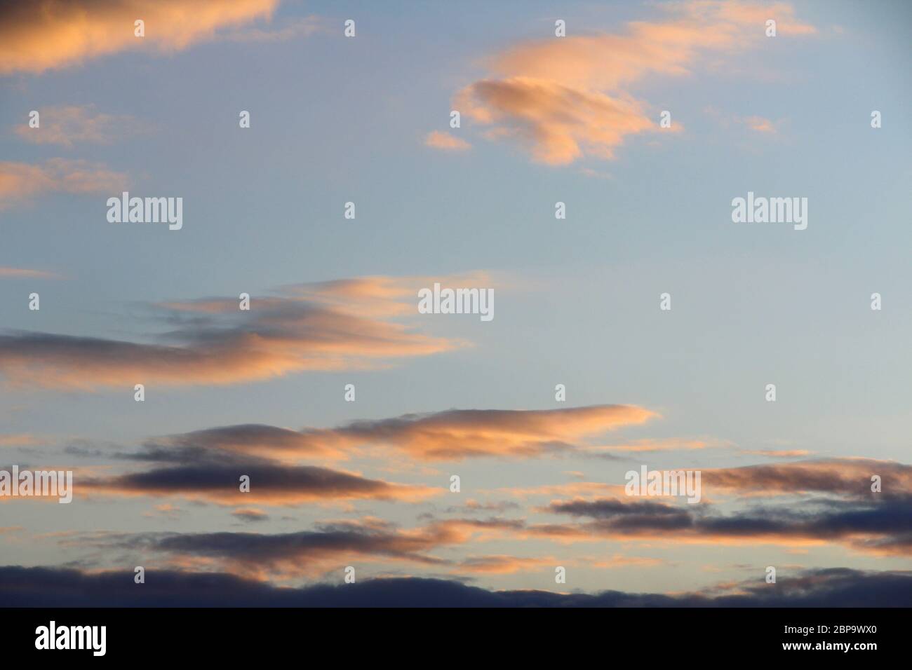 Clouds in the sky are illuminated from below by the red light of the sun. Sunset or sunrise scene at dusk. Stock Photo