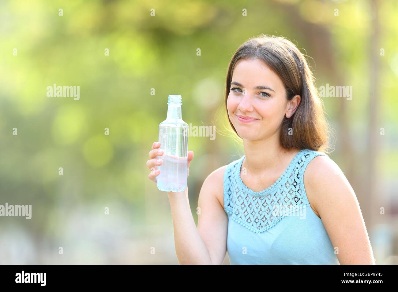Smiley woman holding a bottle of water looking at camera on green ...