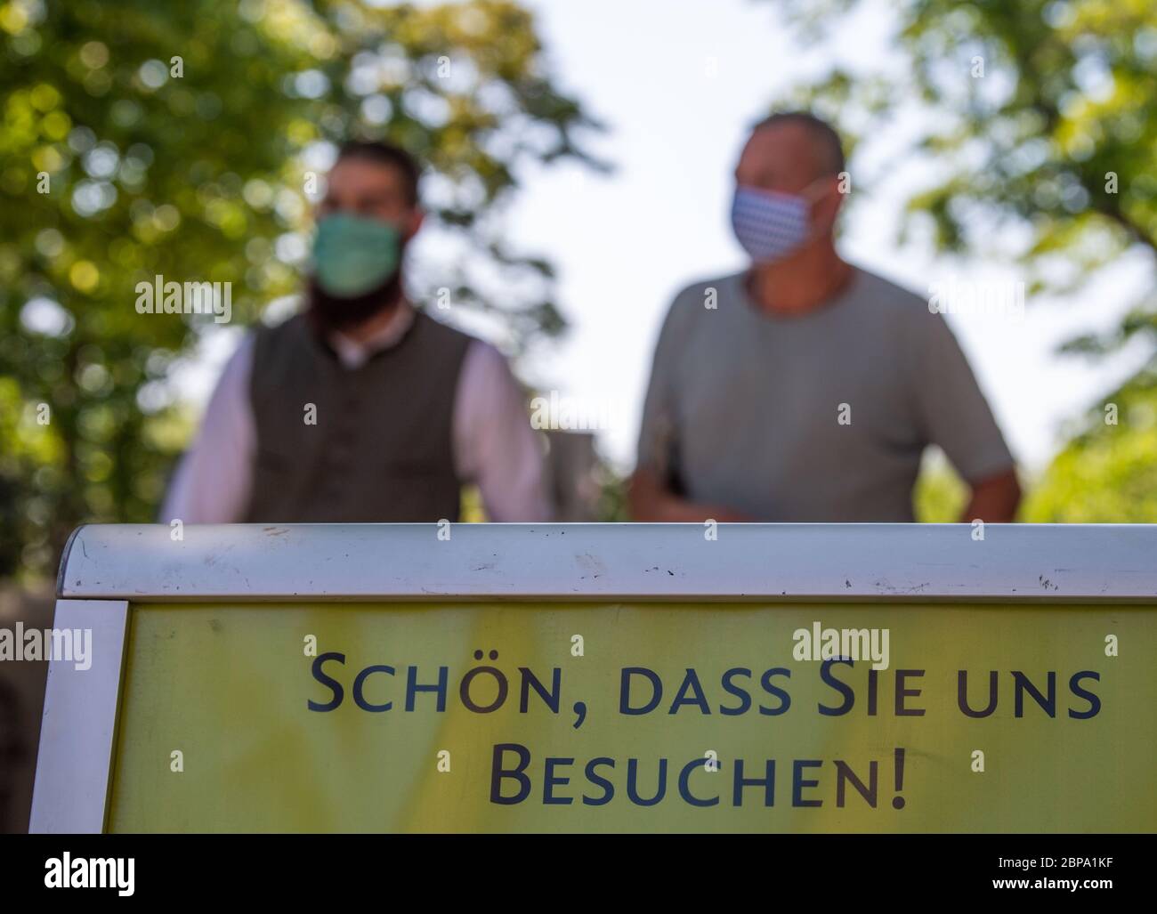 Munich, Germany. 18th May, 2020. Beer garden visitors walk behind a sign saying 'Nice of you to visit us' while wearing mouth-nose protection. Subject to strict hygiene and distance rules, outdoor restaurants in Bavaria are allowed to open again until 8 p.m. after a corona break. Credit: Lino Mirgeler/dpa/Alamy Live News Stock Photo