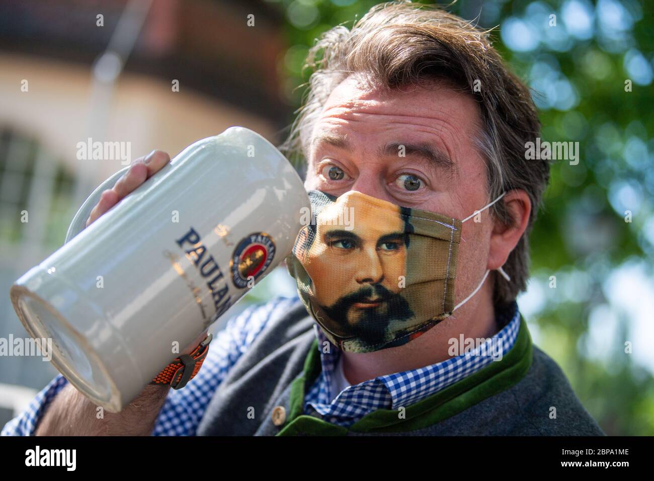 Munich, Germany. 18th May, 2020. Beer garden visitor Harald Kaiser toasts with a stone pitcher while wearing a mouth-and-nose guard with a portrait of King Ludwig. In compliance with strict hygiene and distance rules, outdoor restaurants in Bavaria are allowed to open again until 8 p.m. after a corona break. Credit: Lino Mirgeler/dpa/Alamy Live News Stock Photo