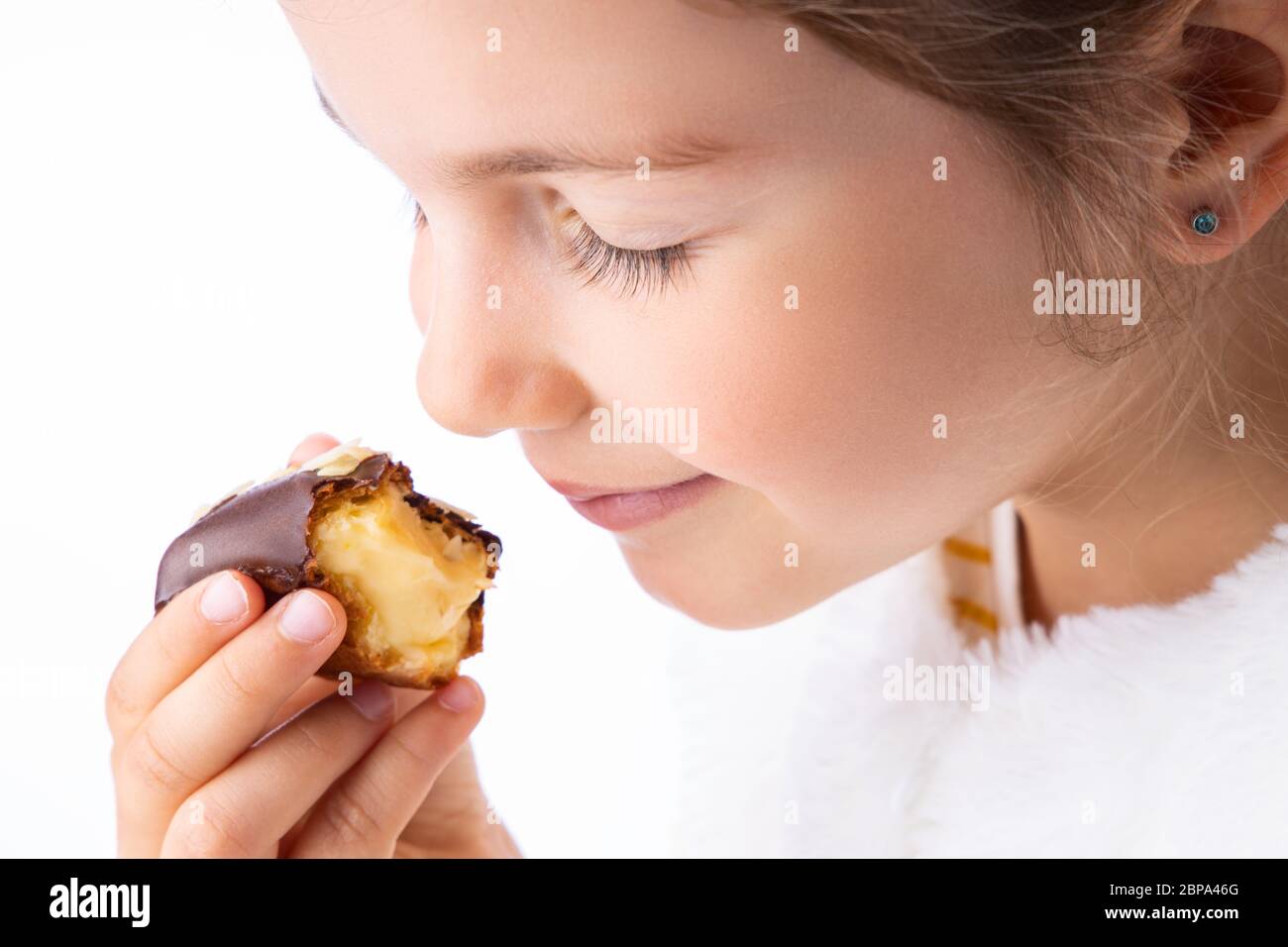 Little girl taste eclair pastry like a pro - smell, bite, eat. Stock Photo