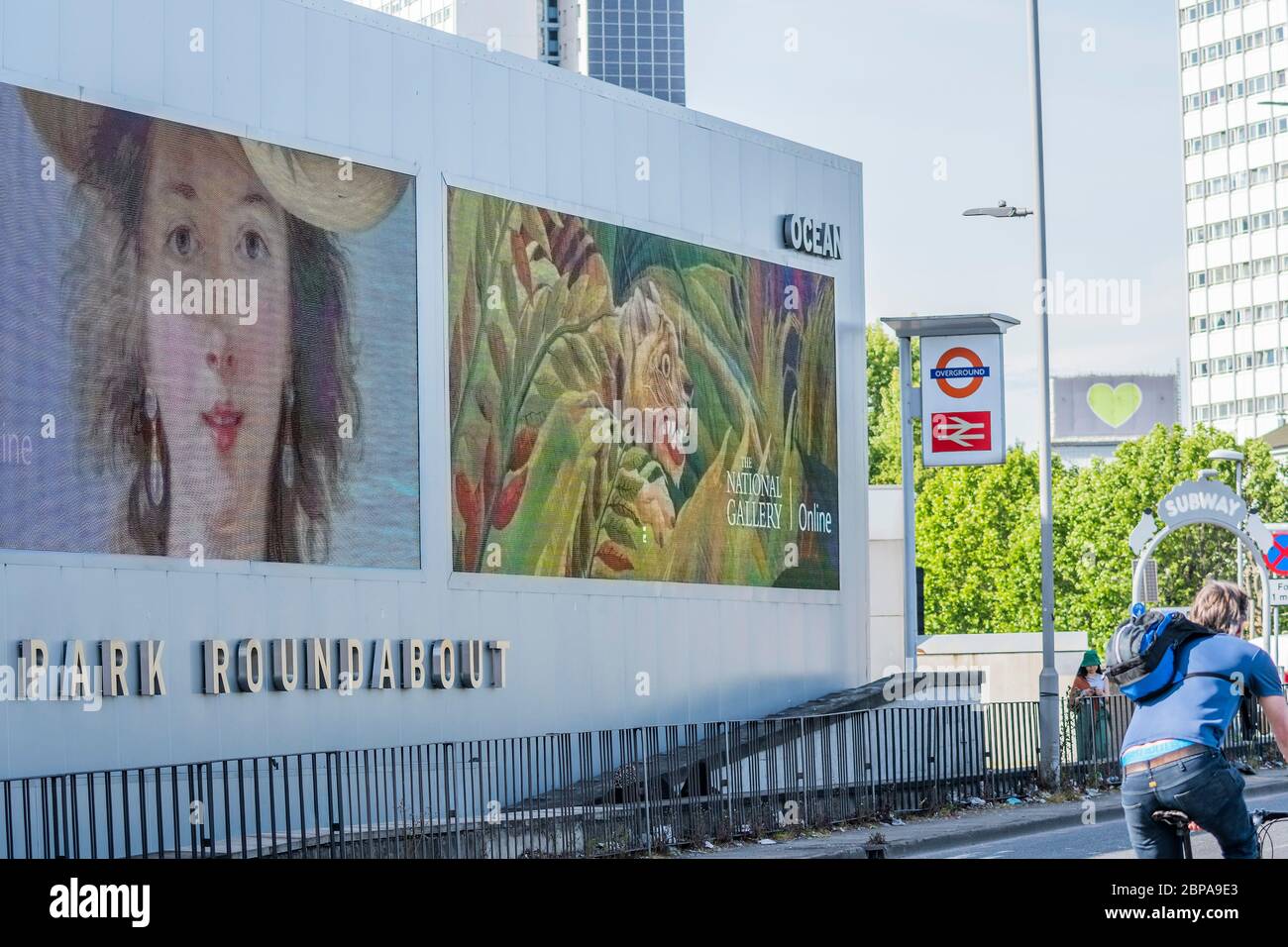 London, UK. 18th May 2020. The National Gallery has teamed up with digital outdoor screen provider, Ocean Outdoor, to bring orks of art out from behind the Gallery's temporarily closed doors (in this case at the Shepherd's Bush Roundabout supersite with the Grenfell Tower heart in the background). The digital sites are free for the next two weeks in order to display images of seven of the Gallery's most iconic paintings: Van Gogh's Sunflowers (1888) and A Wheatfield, with Cypresses (1889), Monet's The Water-Lily Pond (1899), van Eyck's The Arnolfini Portrait (1434), Seurat's Bathers at Asnière Stock Photo