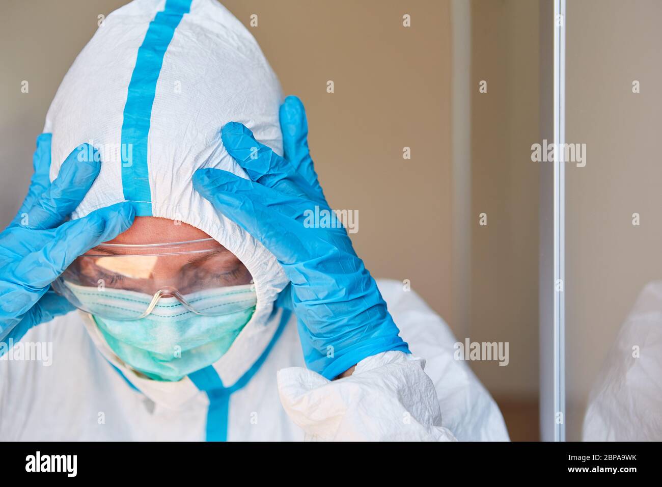 Doctor in protective clothing holds head due to exhaustion or burnout during coronavirus pandemic Stock Photo