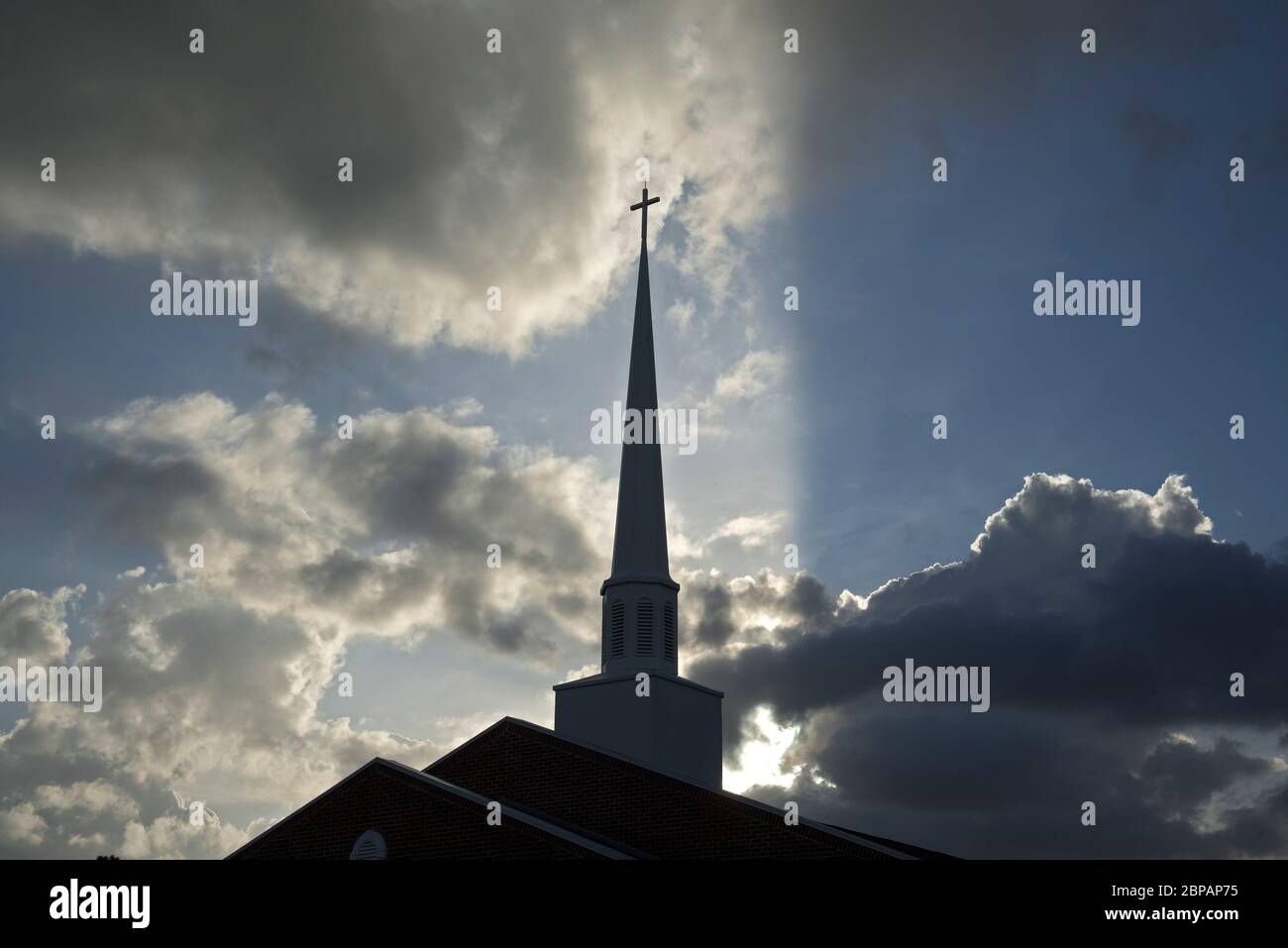 Church Steeple backlit with rays from the setting sun surrounded by magnificent clouds. Stock Photo