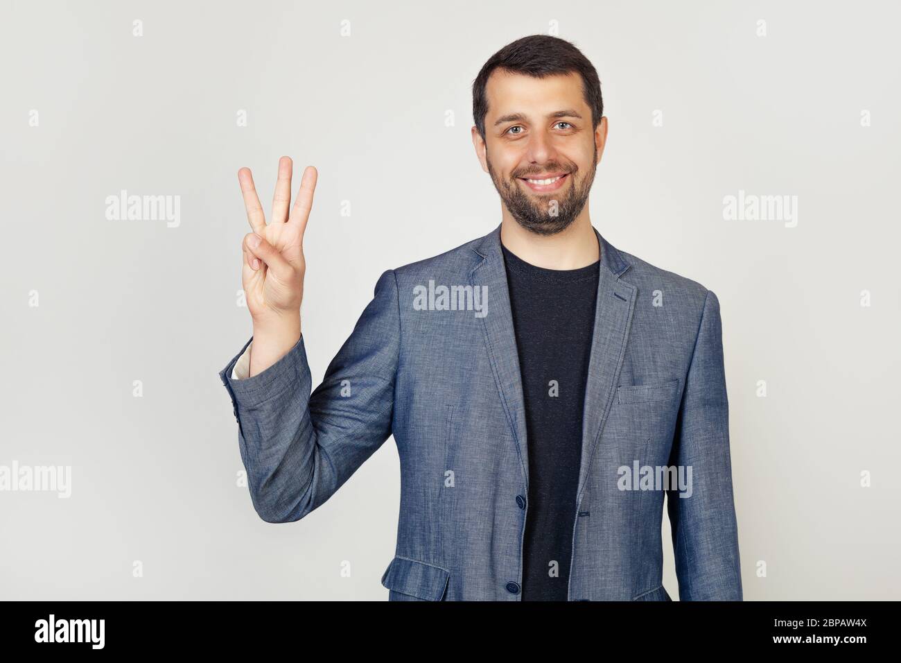 Young businessman with a beard smiles, male businessman in a stylish jacket showing the number three with his fingers, smiling confidently and happy looking at the camera Stock Photo