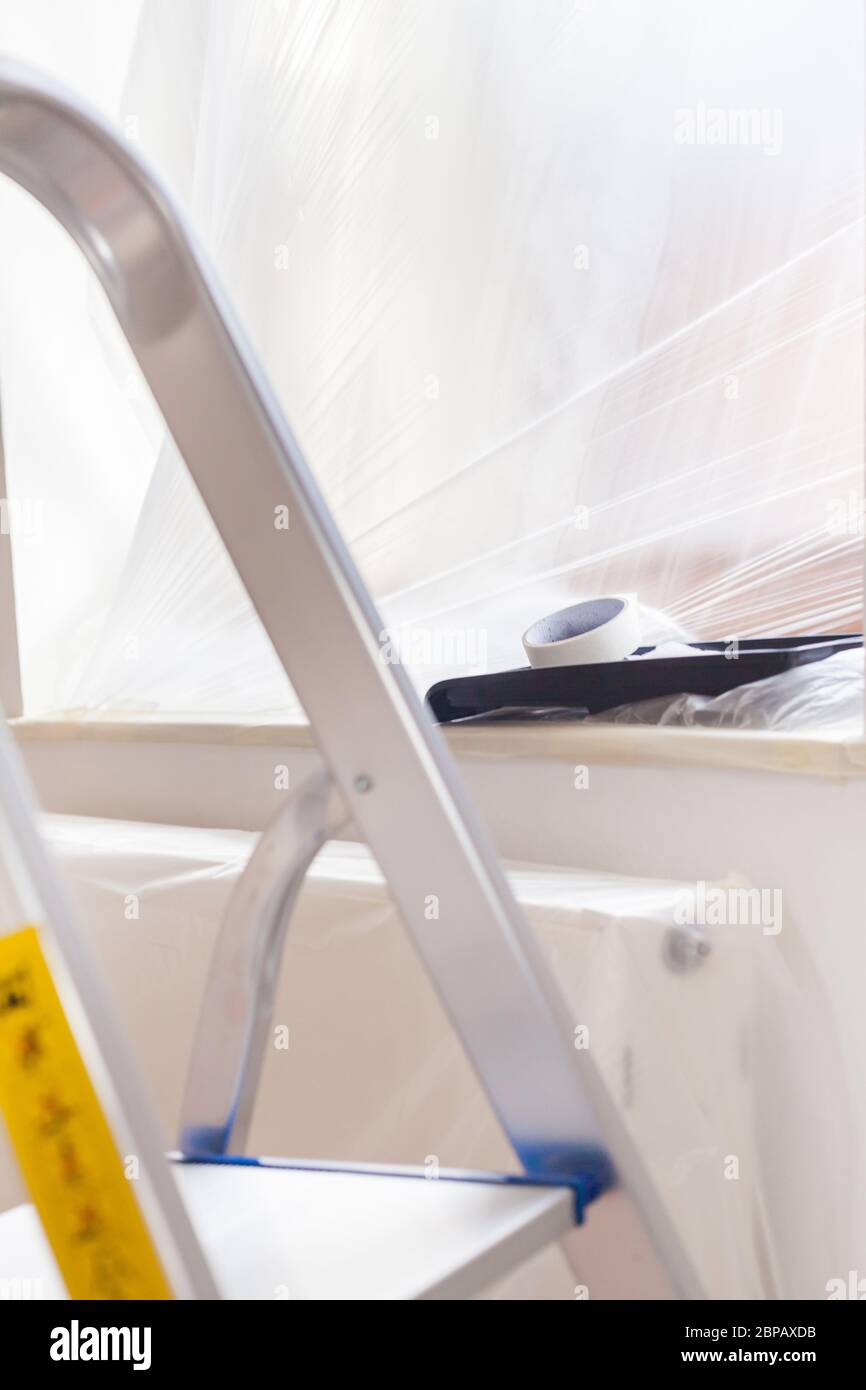 Aluminum ladder is folded out on the taped floor with drip tray craftsman renovation paint preparation do it yourself tools renovated apartment window Stock Photo