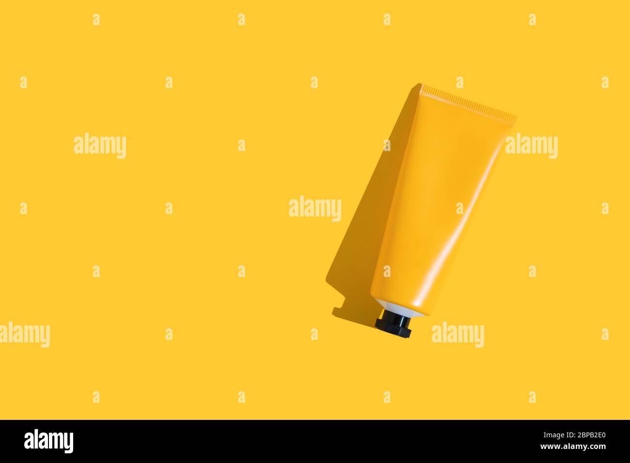 Yellow tube of sunscreen on a bright yellow background with hard shadow ...