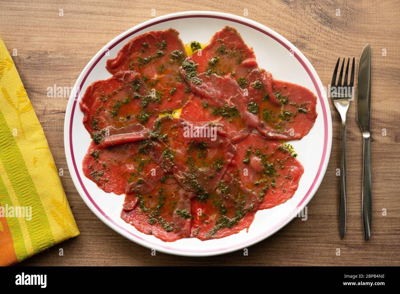 Plate of beef carpaccio with basil marinade on wooden background Stock Photo