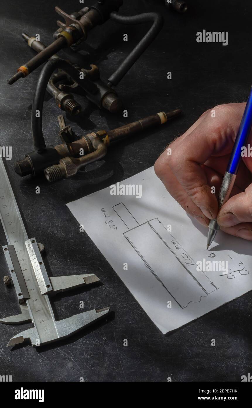 Auto mechanic draws up a drawing on a sheet of paper in a A