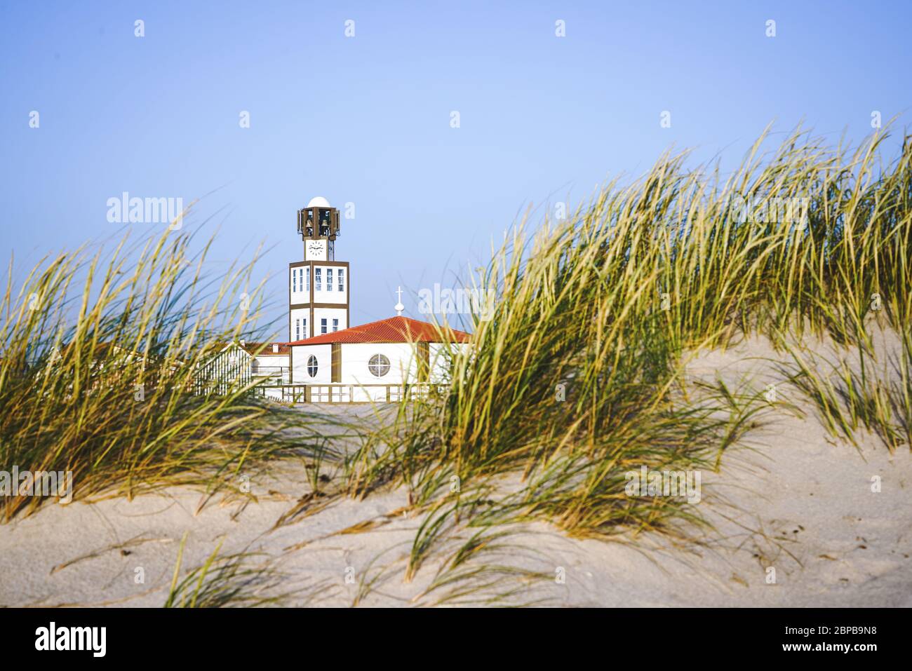 Costa nova church and tower naturally framed with beach sand dunes and sea oats during daylight. Stock Photo