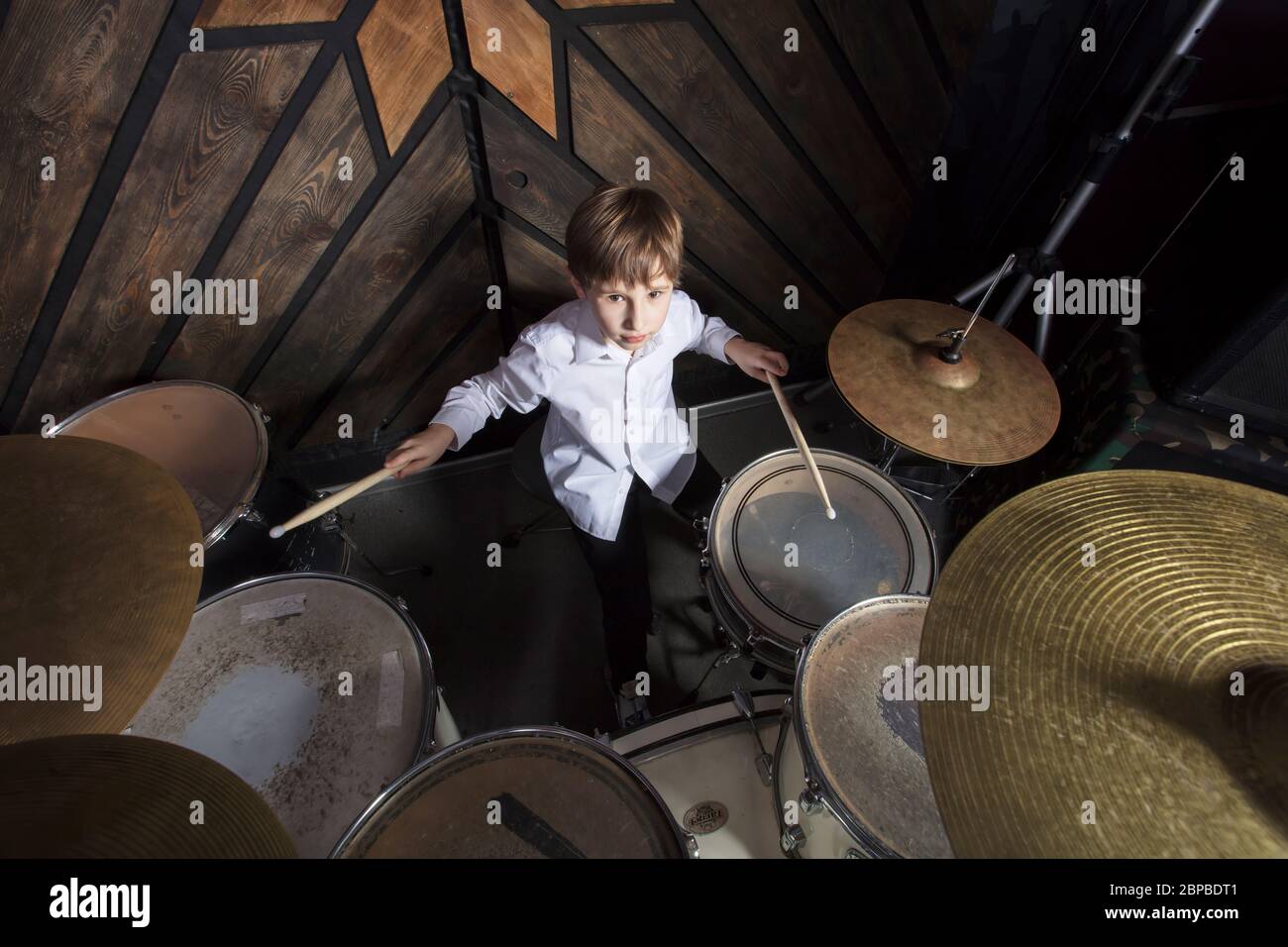 The boy learns to play the drums. The child behind the drum kit. Stock Photo