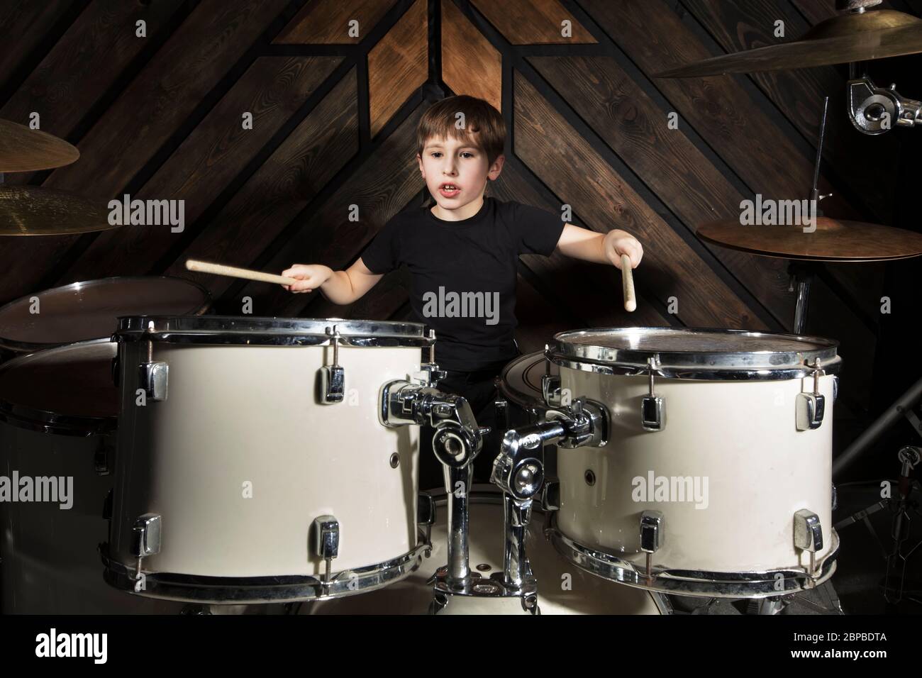 The boy plays the drums. The child behind the drum kit. Stock Photo