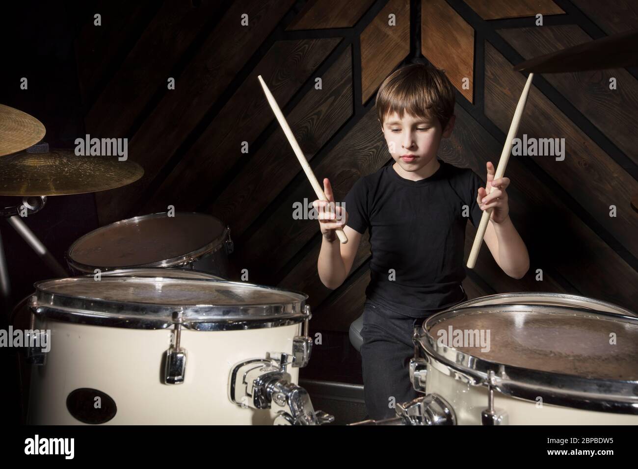 A boy is playing with a drumstick. The child behind the drum kit. Stock Photo