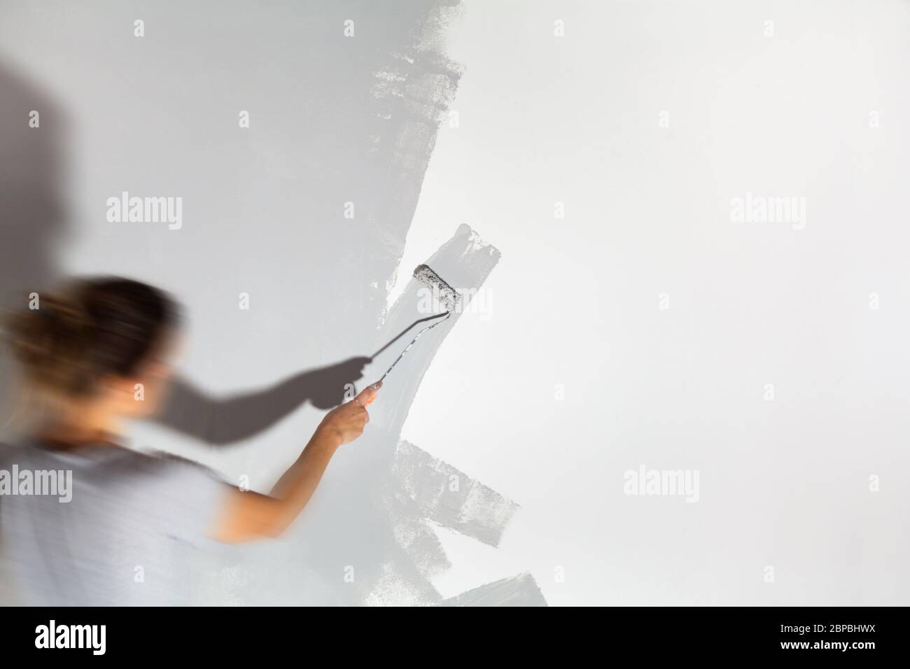 Craftswoman with paint roller paints white wall with silver-gray paint painting company training teaching profession do it yourself tools Stock Photo