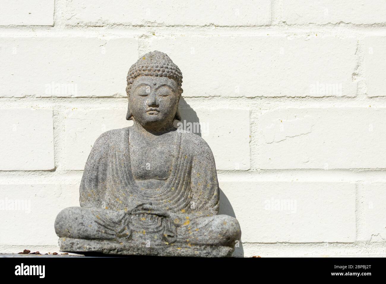 Budha statue sitting in from of white brick wall Stock Photo