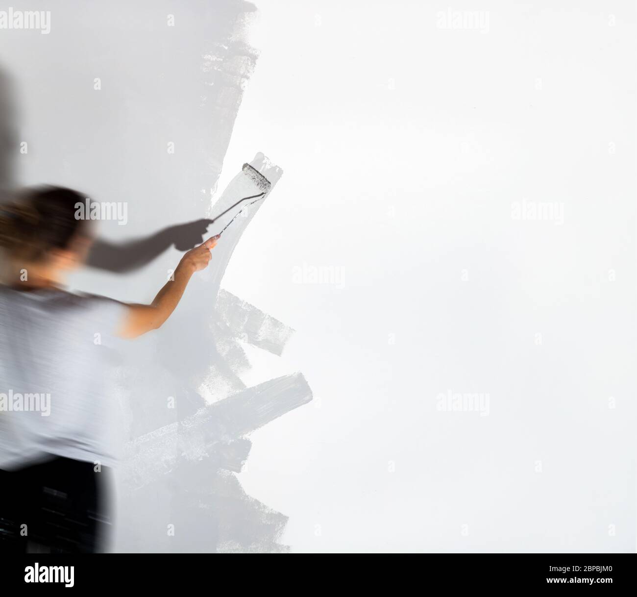 Craftswoman with small paint roller paints white wall with silver-gray paint painting company training teaching profession do it yourself tools Stock Photo