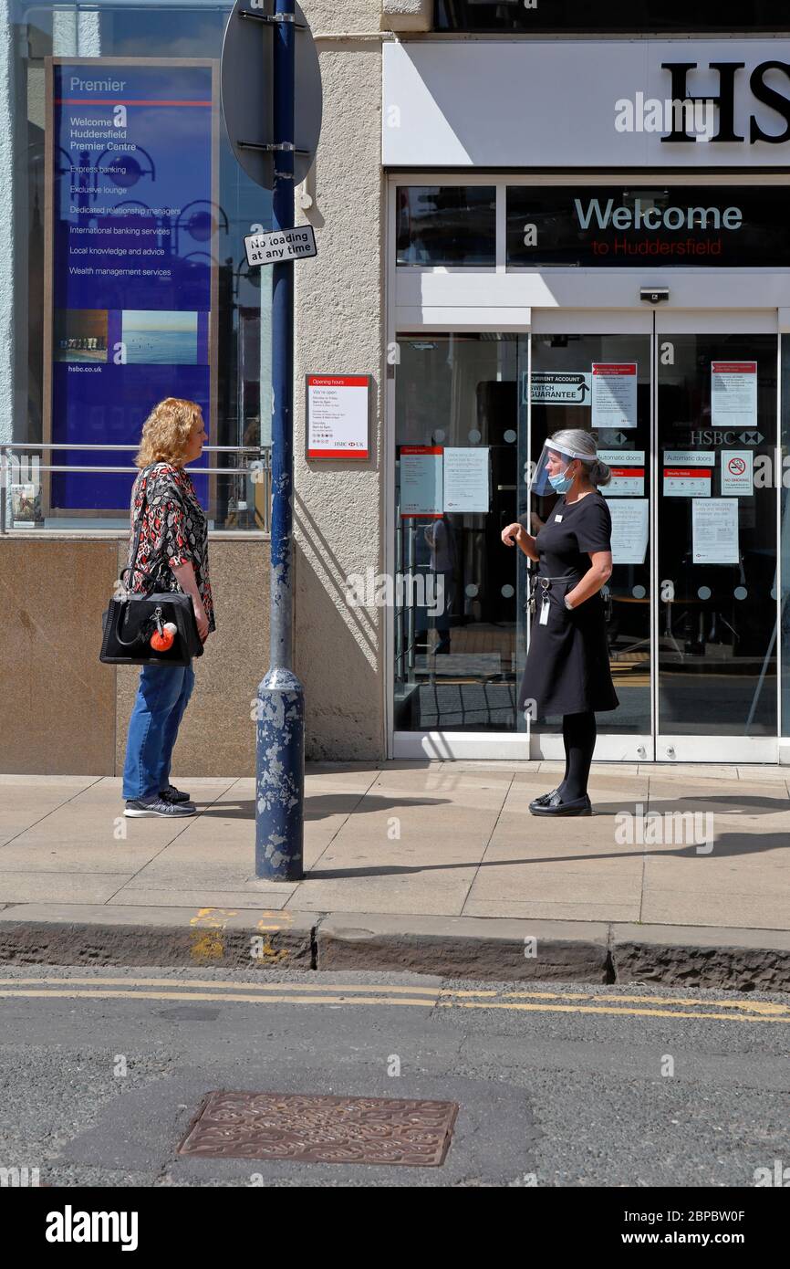 A HSBC bank staff wearing visor and face mask talks to a customer queuing outside the bank during Coronavirus pandemic, West Yorkshire, England, UK. Stock Photo