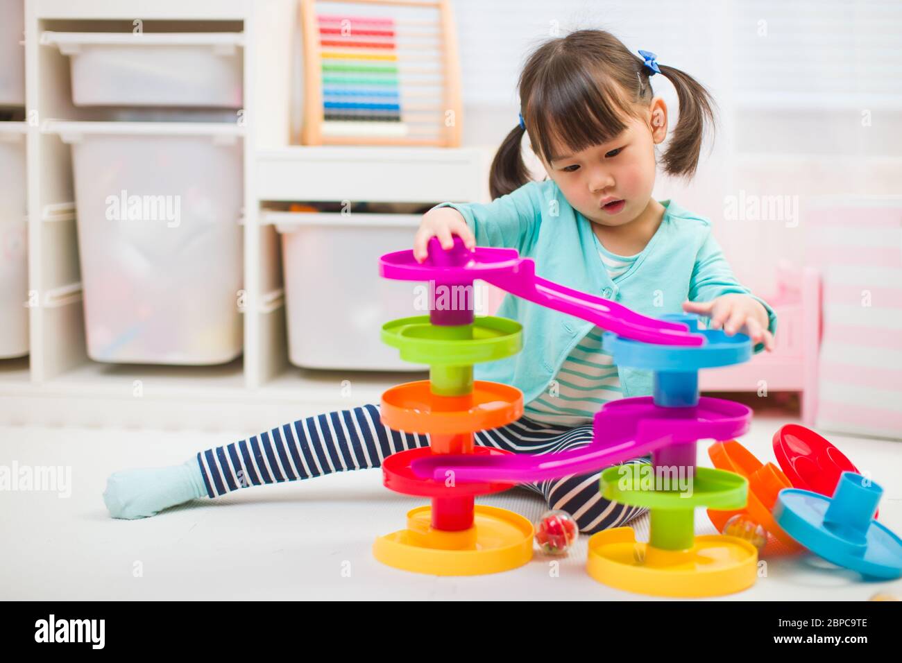 toddler girl play marble run game at gome agianst white background