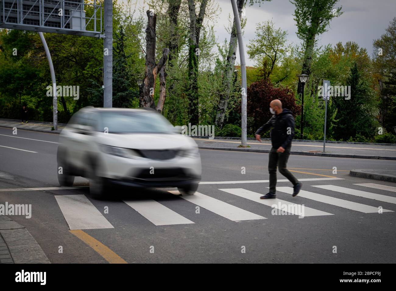 Pedestrian walking on zebra crossing and a driving car failing to stop in blurred motion. Pedestrian reacts with hand to the driver. Stock Photo