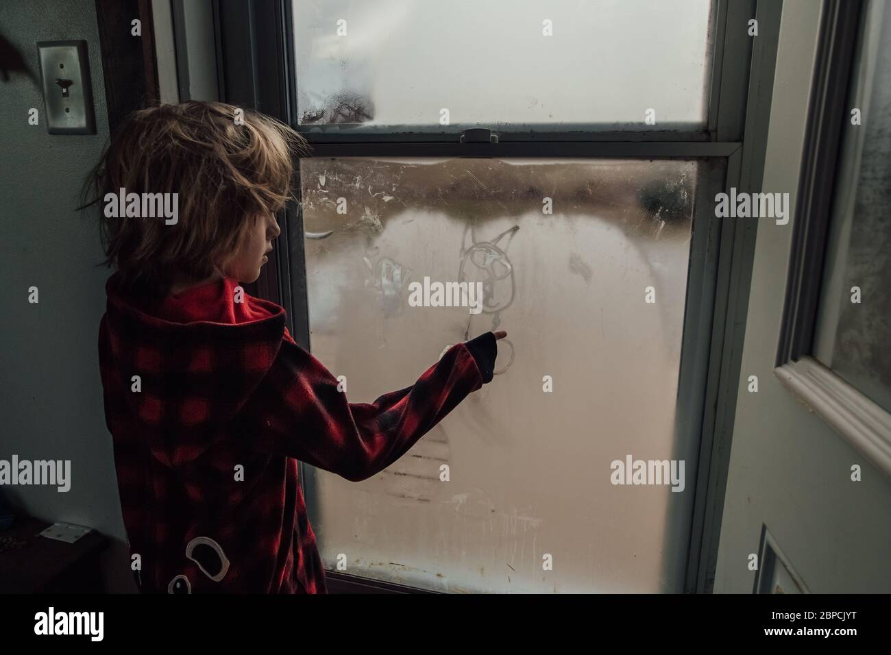 Little boy drawing a picture on the window condensation Stock Photo