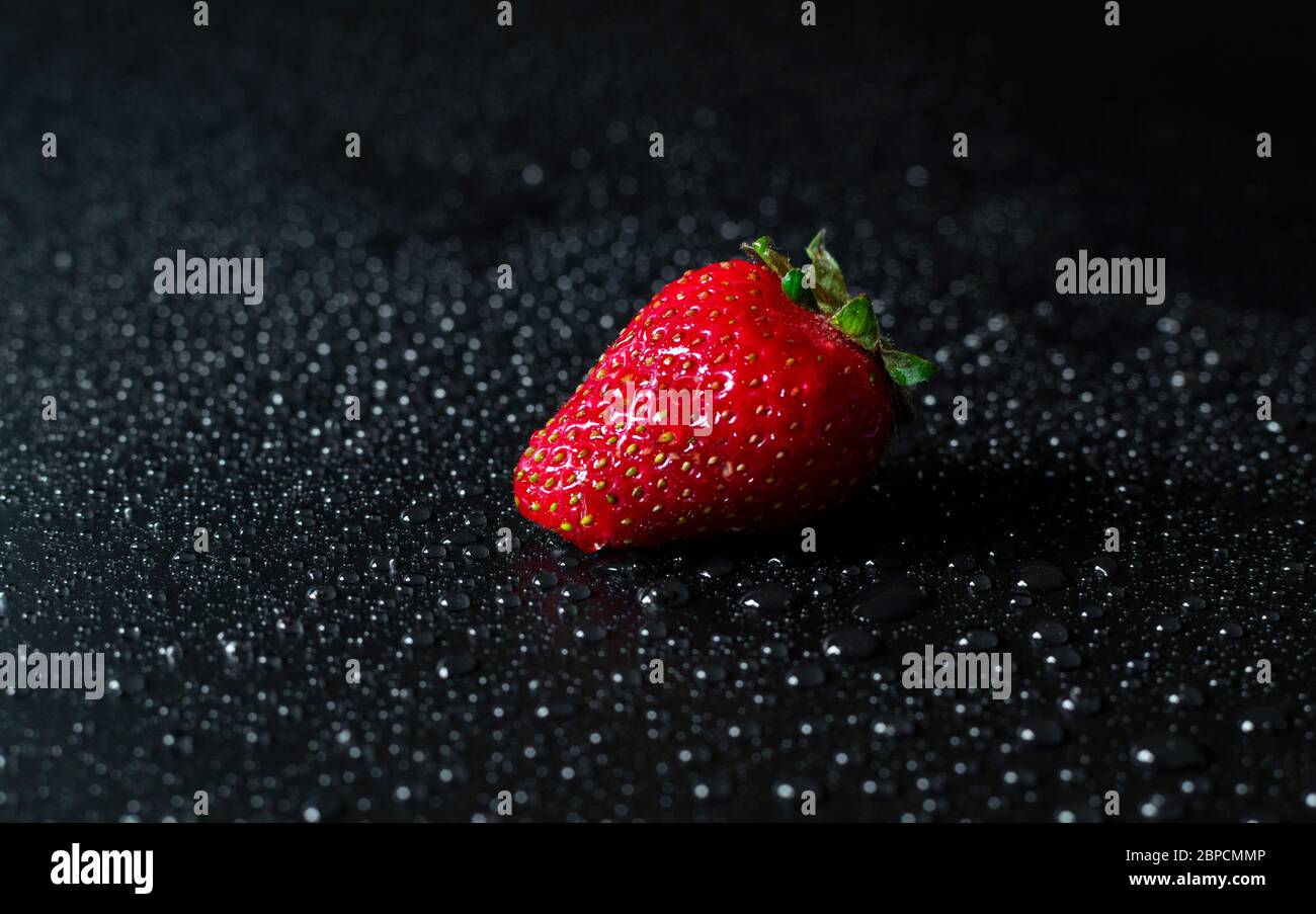 Single fresh and juicy red strawberry on black background with drops of ...