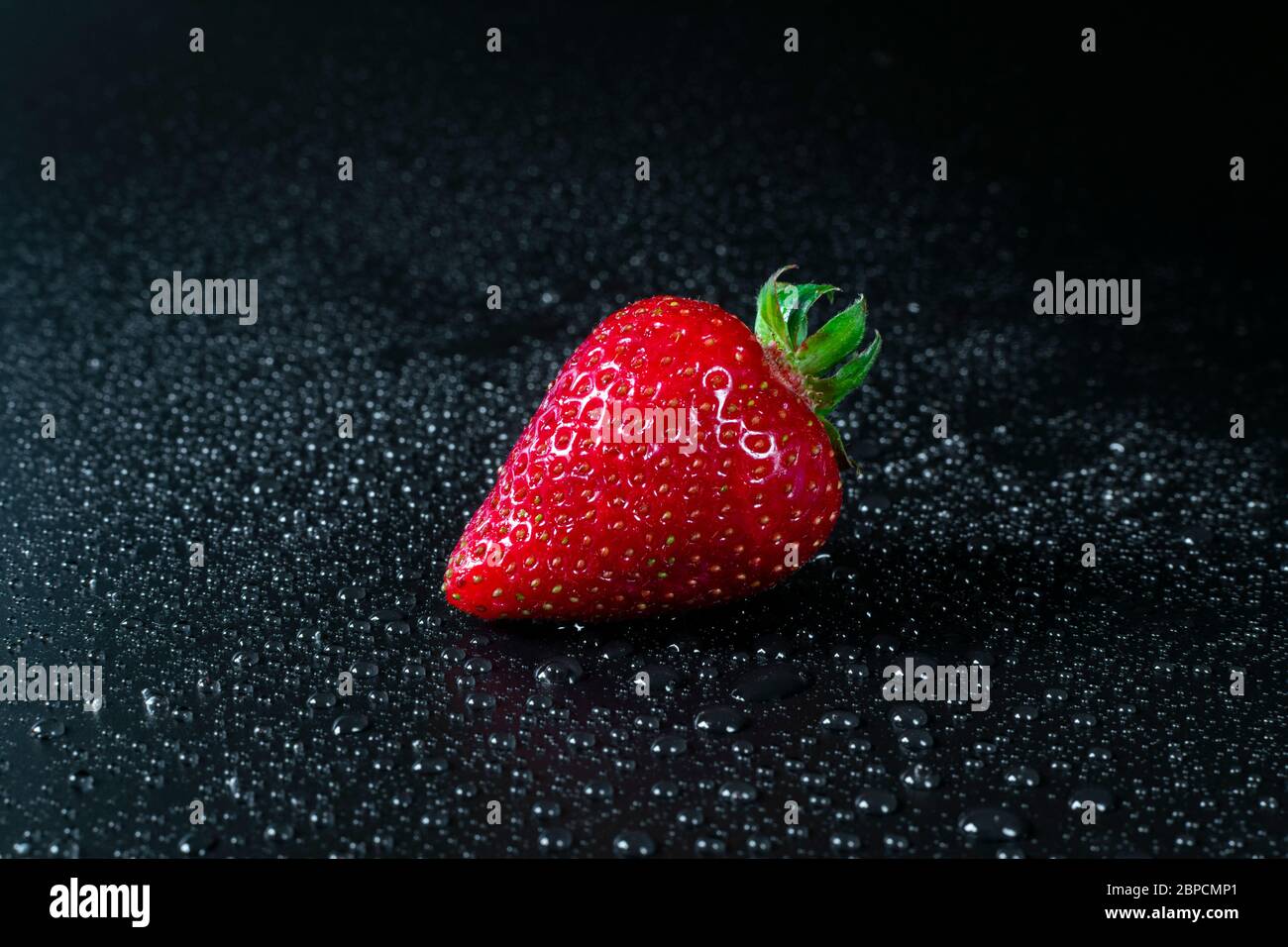 Single fresh and juicy red strawberry on black background with drops of ...