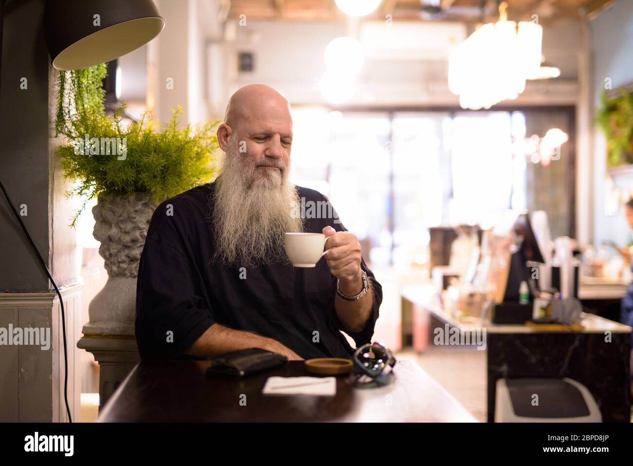 Mature handsome bald bearded man drinking coffee at the coffee shop ...