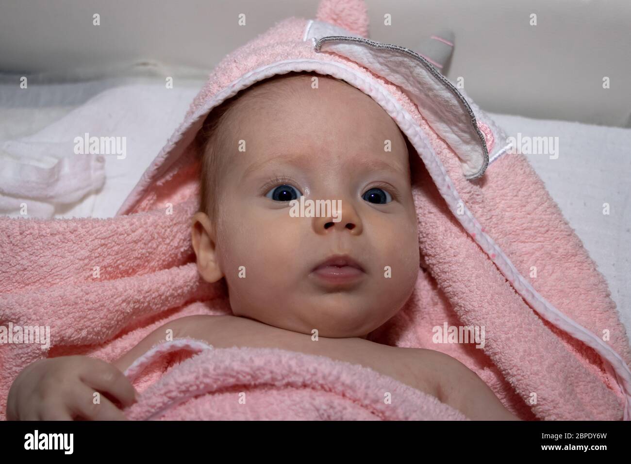 Baby lies on back under the pink towel after bath. 3 months old baby