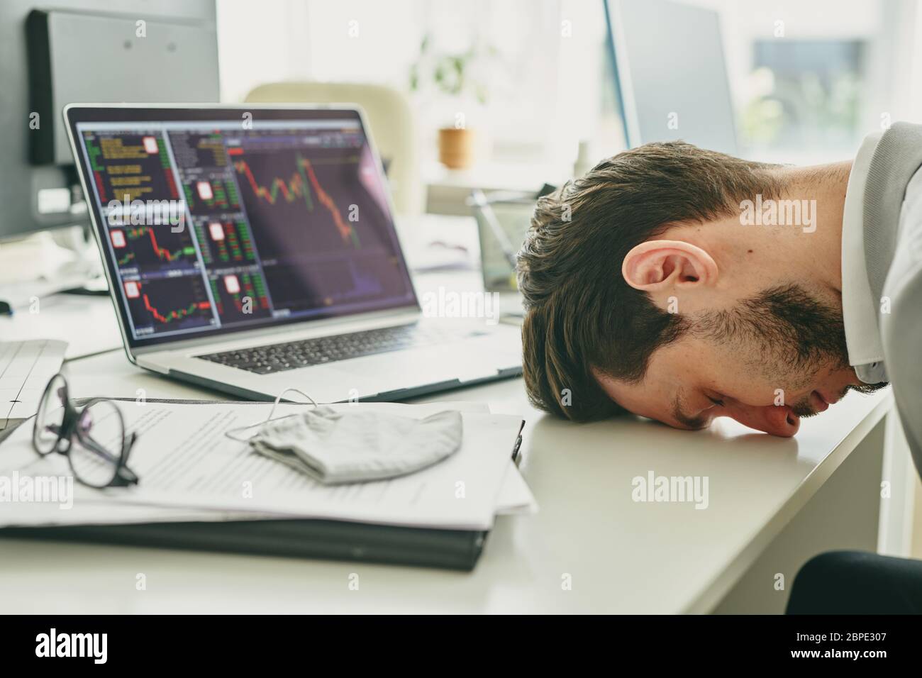 Frustrated young manager banging his head on table after financial analysis of company budget, failure in business during coronavirus Stock Photo