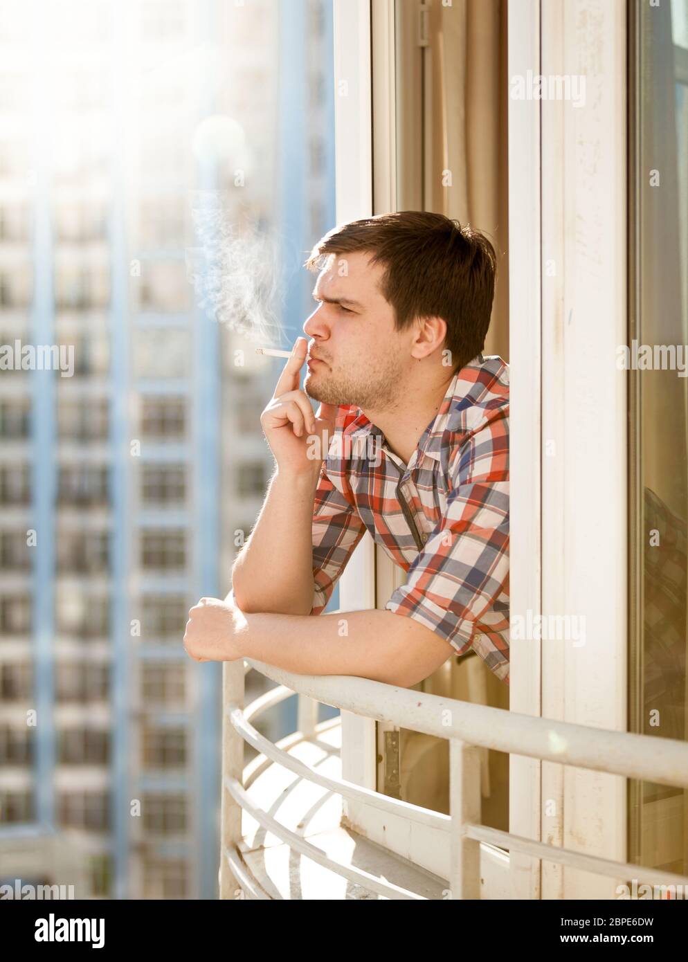 Closeup portrait of young man smoking cigarette out of window Stock